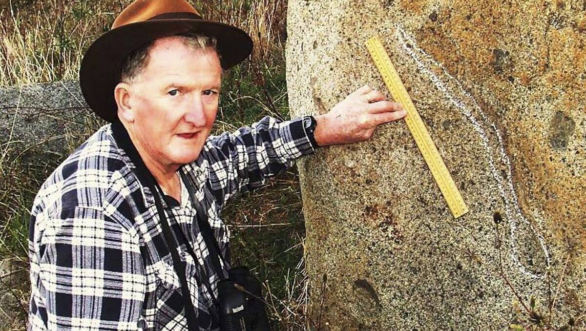 STILL HARD AT IT: Rex Gilroy measures a snake image carved on a Cowra, NSW rockface. Almost 70 years old, he has no plans to retire. 	
