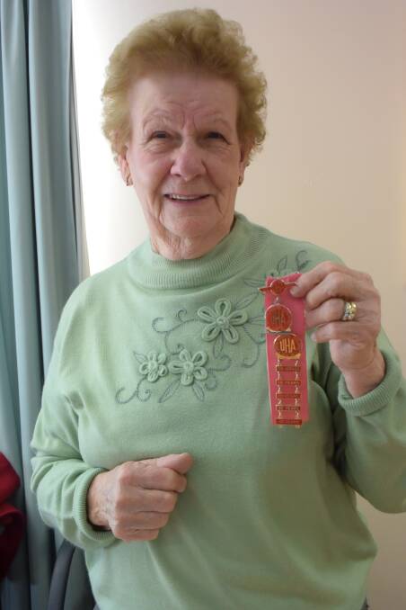 Doreen Mina holding up her life membership badge and her badges for every 10 years she has been part of the club. 