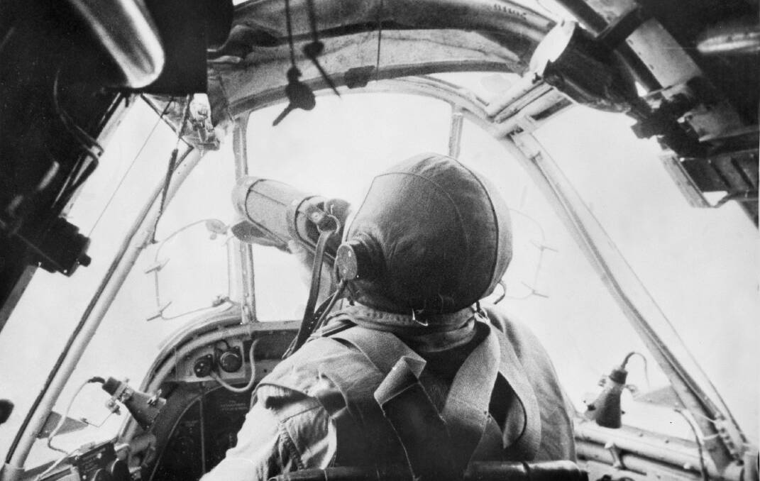 Standing behind the cockpit of an RAAF Beaufighter, war photographer Damien Parer captures Squadron Leader Ron "Torchy" Uren taking a swig from his canteen as the battle rages below. Picture: The Australian War Memorial